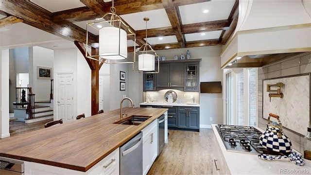 kitchen featuring sink, coffered ceiling, an island with sink, decorative light fixtures, and stainless steel dishwasher