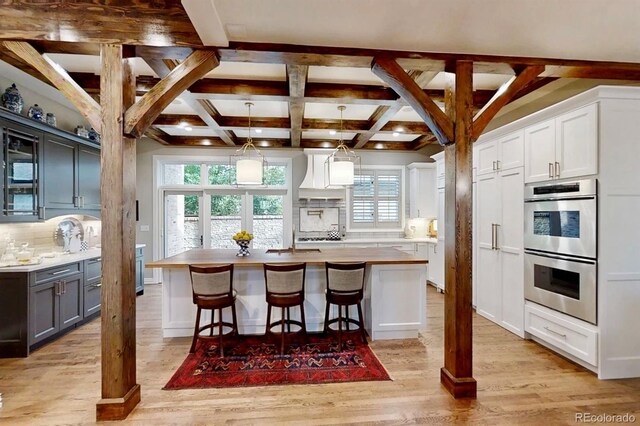 kitchen with double oven, light wood-type flooring, custom range hood, and tasteful backsplash