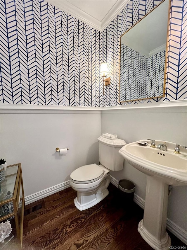 half bath with baseboards, crown molding, toilet, and wood finished floors