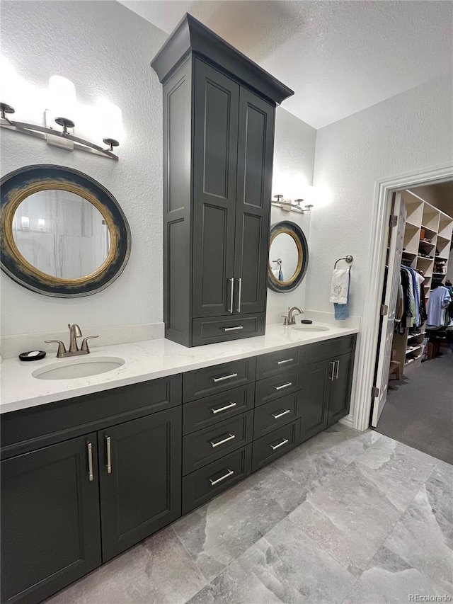 bathroom featuring a textured wall, double vanity, a sink, and a walk in closet