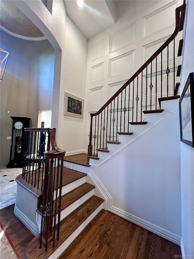 stairway featuring arched walkways, wood finished floors, and baseboards