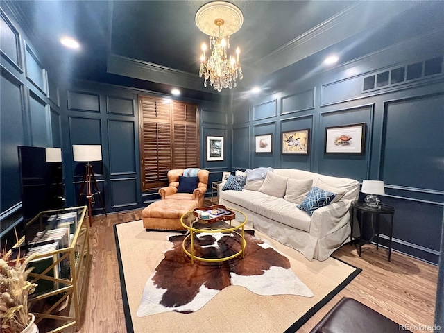 living room with a decorative wall, wood finished floors, ornamental molding, a tray ceiling, and an inviting chandelier