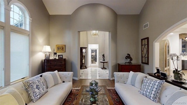 living room with a high ceiling, wood finished floors, visible vents, baseboards, and an inviting chandelier