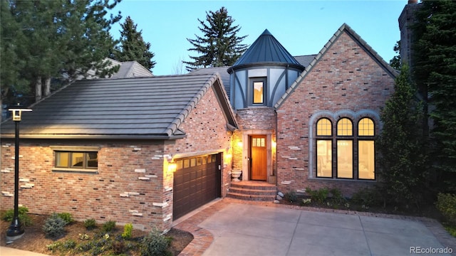 english style home with metal roof, an attached garage, brick siding, concrete driveway, and a standing seam roof