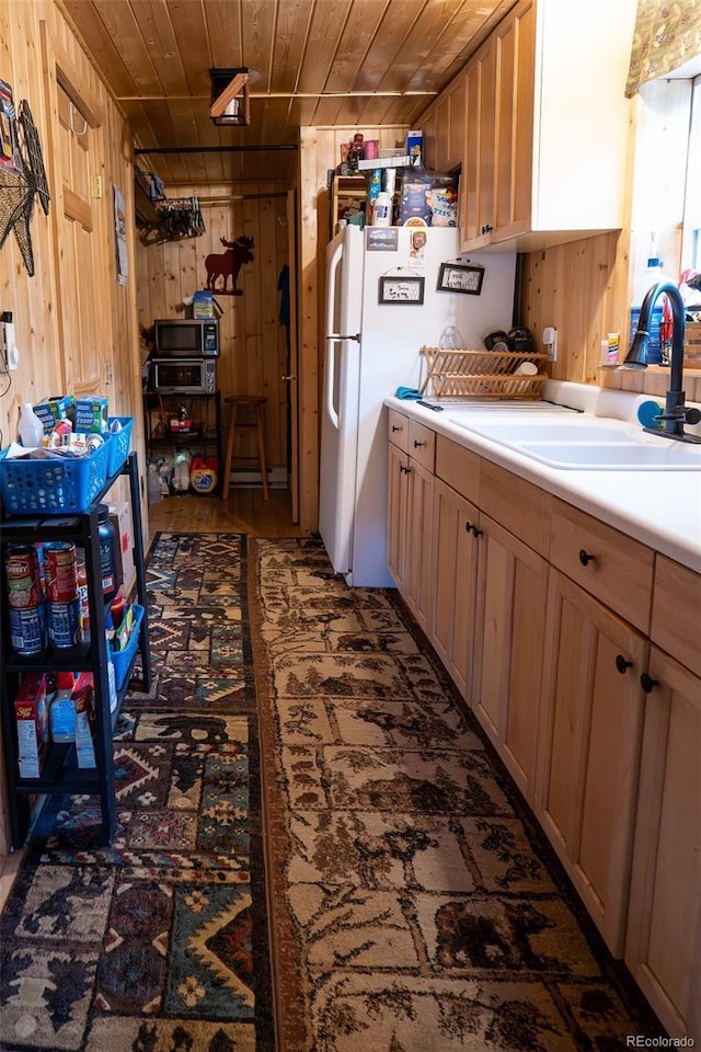 kitchen featuring wooden walls, wood ceiling, freestanding refrigerator, light countertops, and a sink