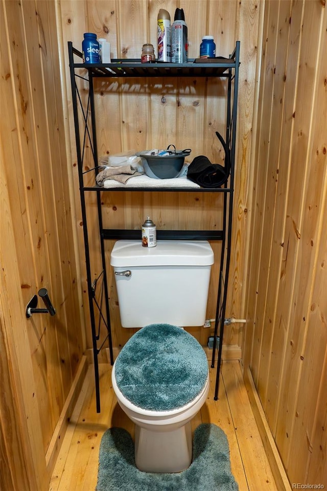 half bathroom with toilet, wooden walls, and hardwood / wood-style floors