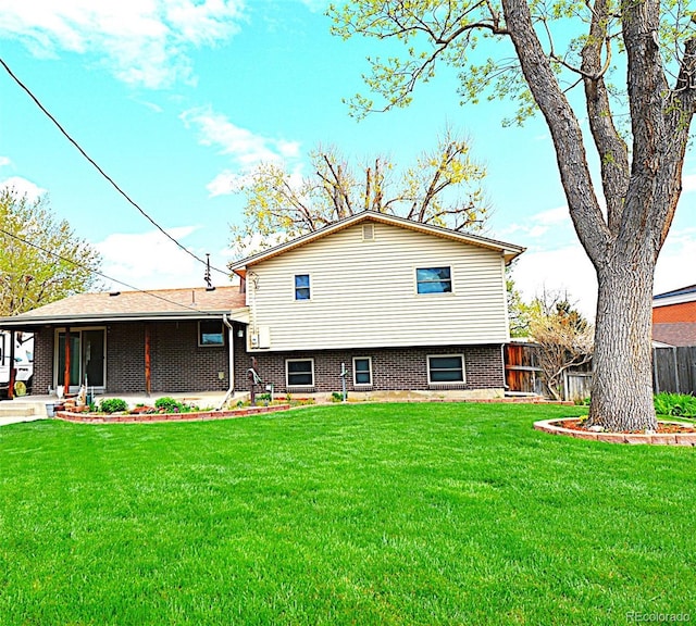 back of house featuring a lawn, fence, and brick siding
