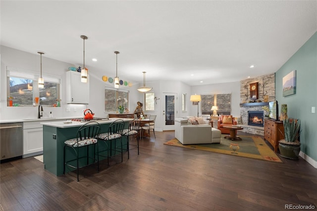 kitchen featuring dishwasher, a breakfast bar, white cabinets, a stone fireplace, and a kitchen island