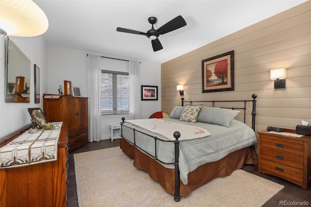 bedroom with hardwood / wood-style floors, ceiling fan, and wooden walls