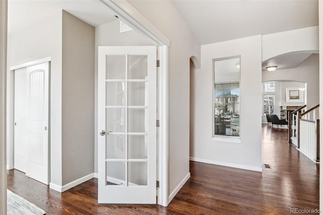 corridor featuring arched walkways, visible vents, baseboards, and dark wood-style flooring