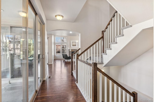 foyer featuring stairway, visible vents, baseboards, arched walkways, and dark wood-type flooring