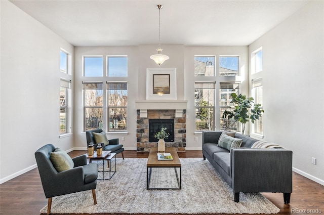 living area featuring a stone fireplace, a high ceiling, baseboards, and wood finished floors