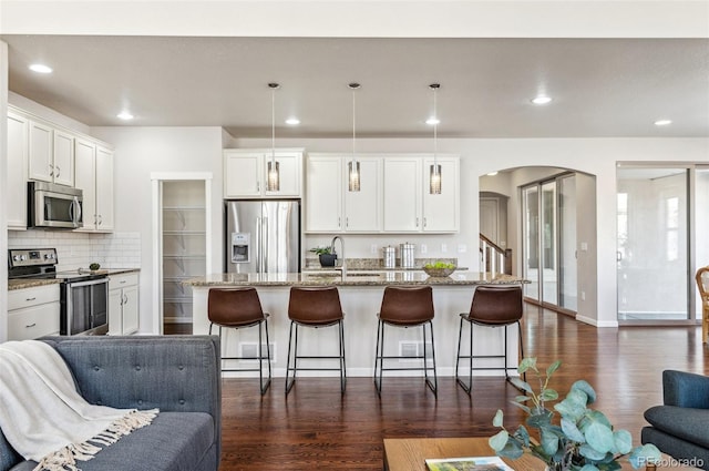 kitchen with a sink, open floor plan, stainless steel appliances, arched walkways, and dark wood-style flooring