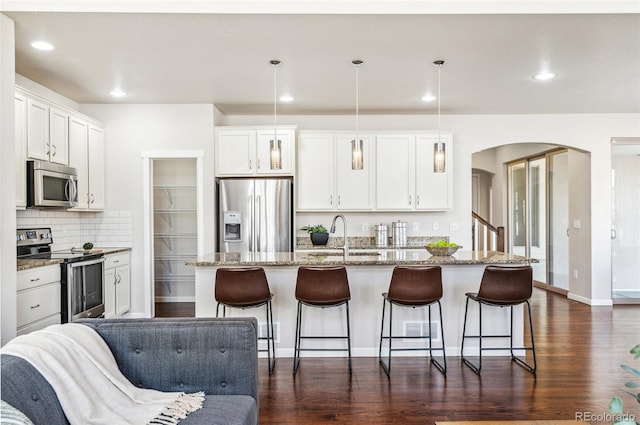 kitchen featuring dark wood finished floors, arched walkways, a sink, stainless steel appliances, and a kitchen breakfast bar