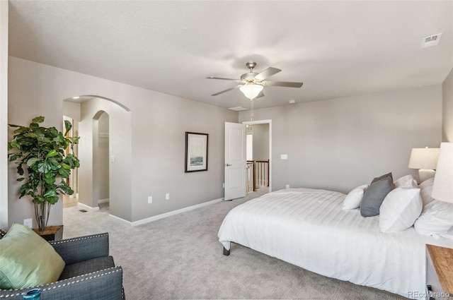 bedroom featuring visible vents, a ceiling fan, arched walkways, baseboards, and light colored carpet