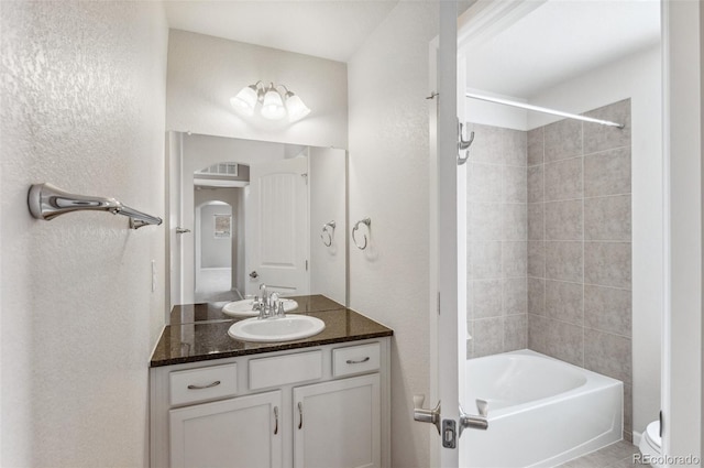 bathroom with toilet, vanity, bathtub / shower combination, and a textured wall