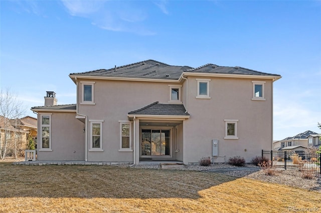 back of house featuring fence, a yard, a chimney, stucco siding, and a tile roof