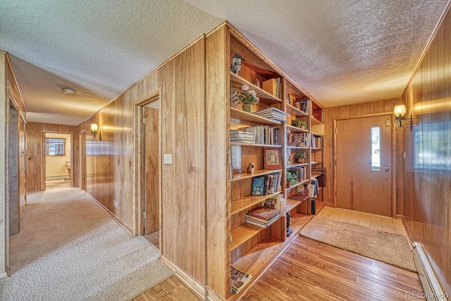 hall with wood walls, light wood-type flooring, and a textured ceiling