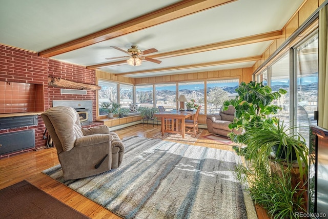 sunroom / solarium featuring a mountain view, a fireplace, ceiling fan, and beamed ceiling