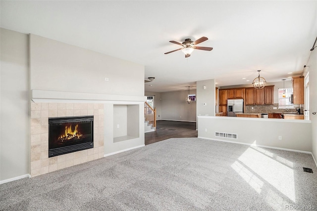 11748 Mill Valley St, Parker, CO 80138 - unfurnished living room featuring dark colored carpet, a tiled fireplace, ceiling fan, stairs, and baseboards