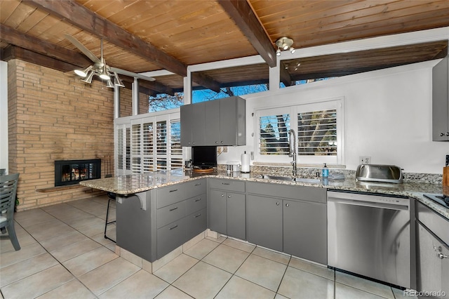 kitchen featuring kitchen peninsula, stainless steel dishwasher, stone counters, gray cabinets, and a stone fireplace