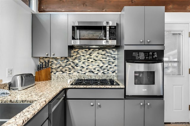 kitchen featuring gray cabinetry, decorative backsplash, light stone countertops, and appliances with stainless steel finishes