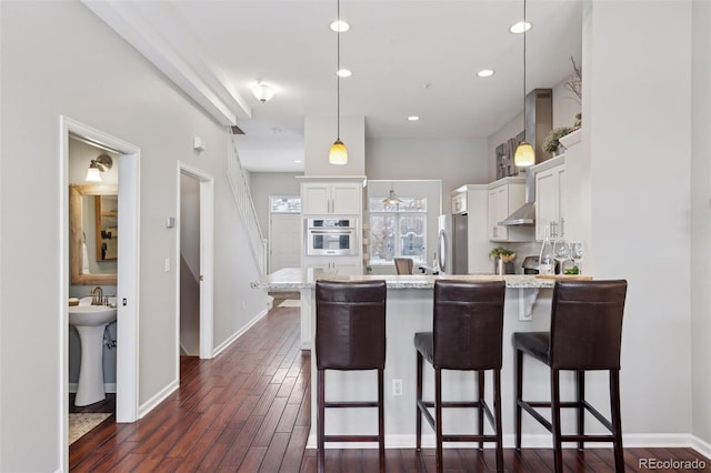 kitchen with white cabinets, a kitchen bar, dark wood-type flooring, stainless steel appliances, and hanging light fixtures