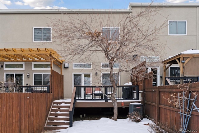 snow covered rear of property with a wooden deck, cooling unit, and a pergola