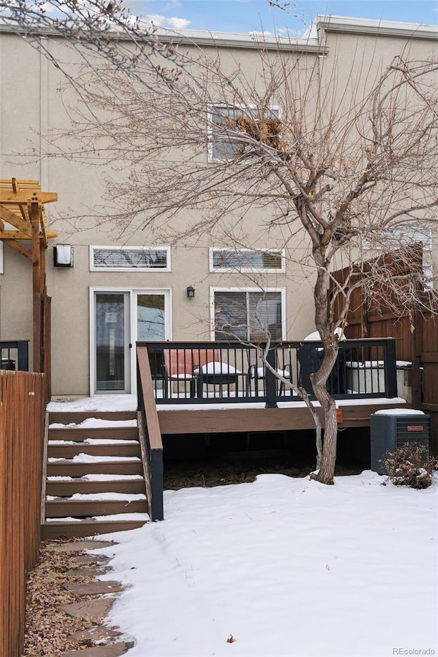 snow covered back of property with a deck and central AC