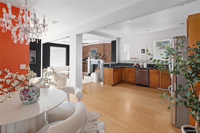 kitchen with light hardwood / wood-style flooring, a brick fireplace, appliances with stainless steel finishes, and an inviting chandelier