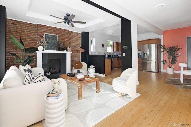 living room featuring light wood-type flooring, a raised ceiling, ceiling fan, and brick wall