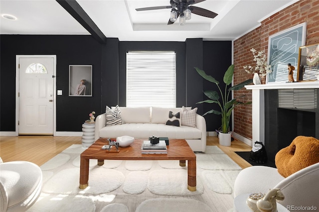 living room with light wood-type flooring, a tray ceiling, ceiling fan, and brick wall