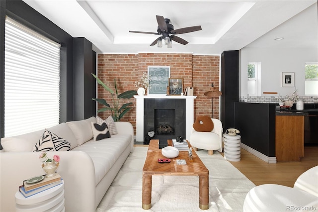 living room with a raised ceiling, light hardwood / wood-style floors, ceiling fan, and brick wall