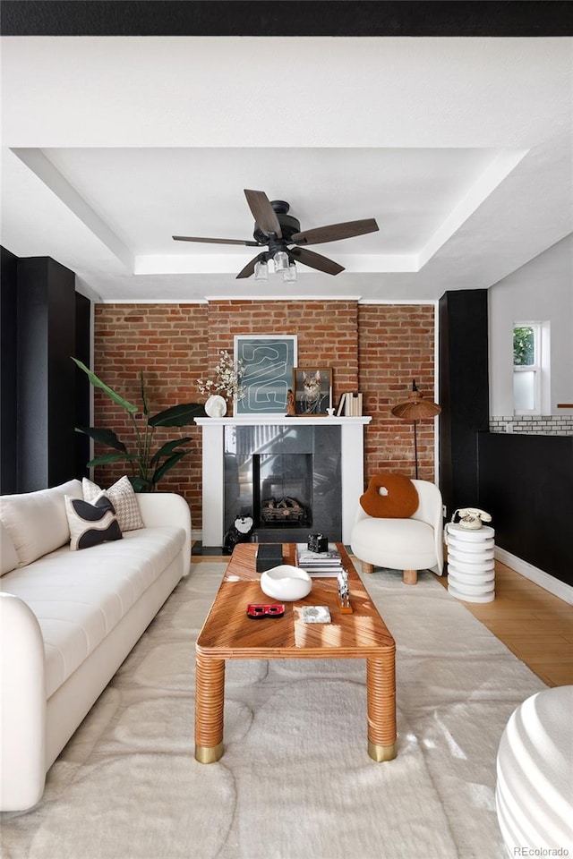 living room with light hardwood / wood-style flooring, a tray ceiling, ceiling fan, and brick wall