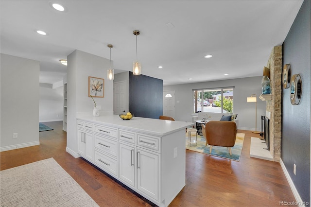 kitchen with decorative light fixtures, a stone fireplace, wood-type flooring, and white cabinetry