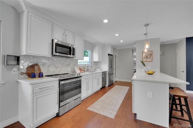 kitchen with pendant lighting, light wood-type flooring, white cabinetry, and appliances with stainless steel finishes