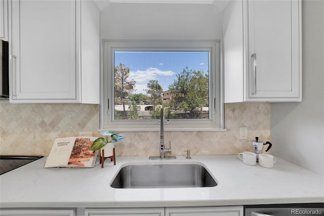 kitchen with white cabinets, backsplash, light stone countertops, and sink