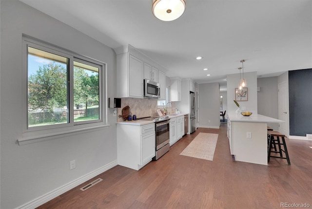 kitchen featuring white cabinetry, dark wood-type flooring, pendant lighting, a breakfast bar, and appliances with stainless steel finishes