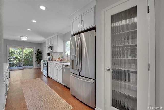 kitchen with white cabinetry, sink, stainless steel appliances, light hardwood / wood-style flooring, and backsplash