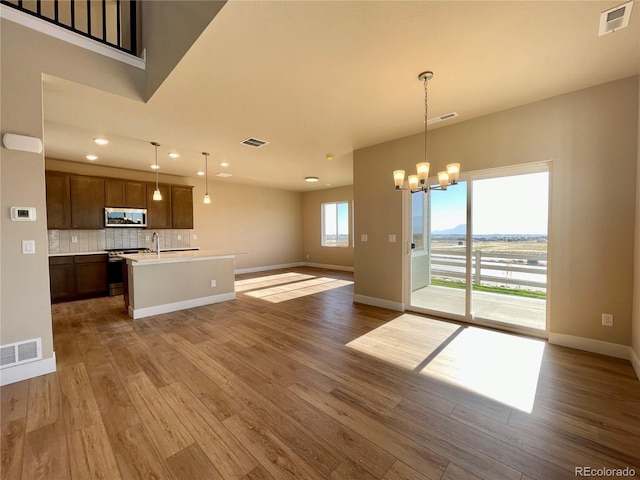 kitchen featuring appliances with stainless steel finishes, backsplash, decorative light fixtures, a center island with sink, and hardwood / wood-style floors