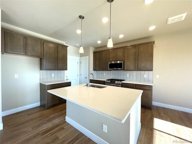 kitchen with stainless steel appliances, a center island with sink, a sink, and light countertops