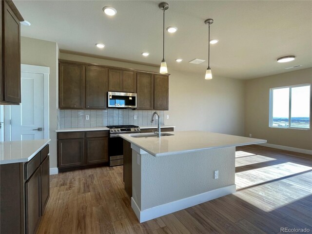 kitchen with decorative backsplash, appliances with stainless steel finishes, a kitchen island with sink, sink, and hanging light fixtures