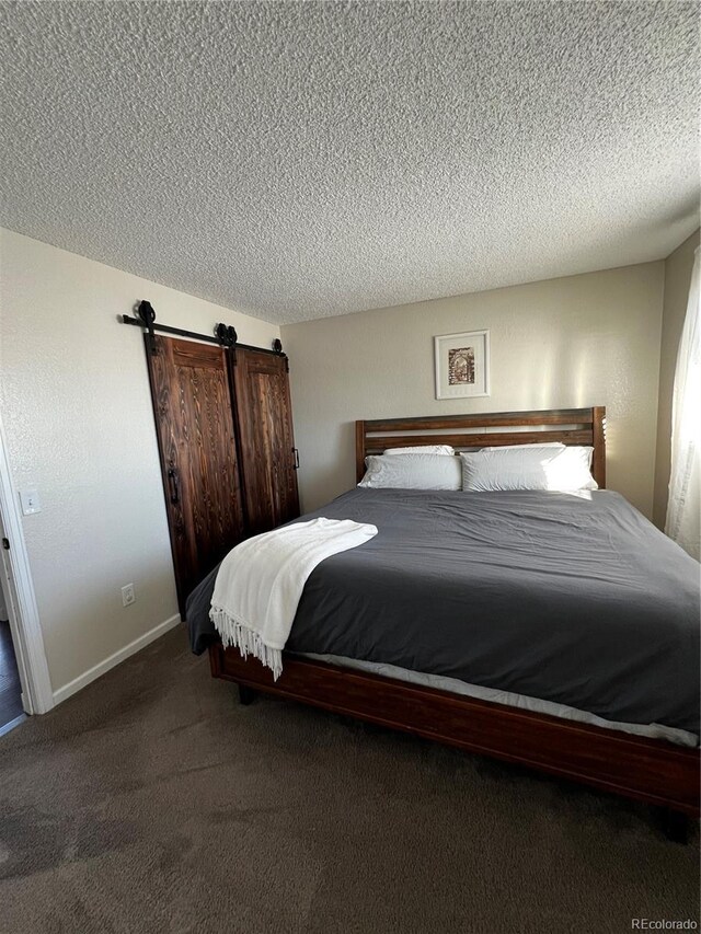 bedroom featuring dark colored carpet, a textured ceiling, and a barn door