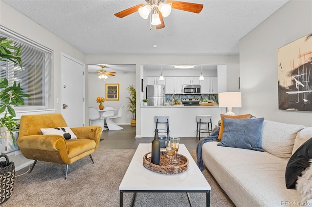 living area featuring a ceiling fan, a textured ceiling, and baseboards