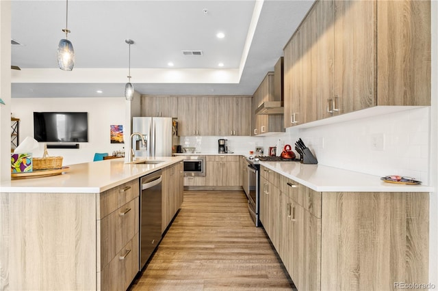kitchen featuring modern cabinets, a sink, light brown cabinets, stainless steel appliances, and wall chimney exhaust hood