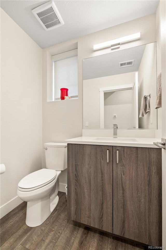 half bathroom featuring toilet, baseboards, visible vents, and wood finished floors