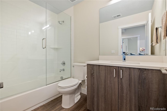 full bathroom featuring shower / bath combination with glass door, vanity, toilet, wood finished floors, and visible vents