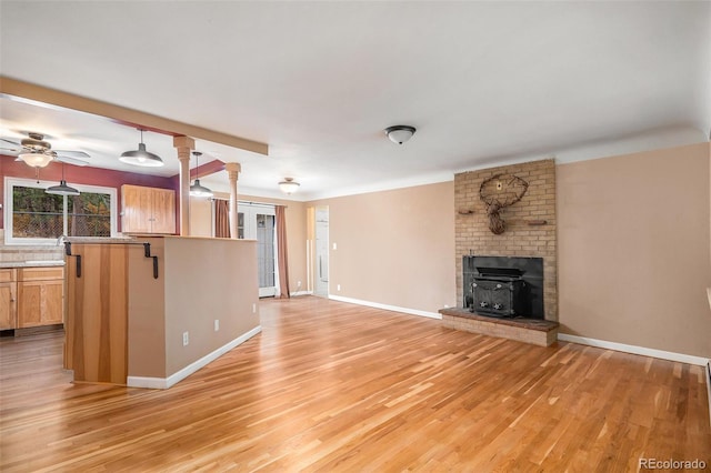 unfurnished living room with ornate columns, light hardwood / wood-style floors, a wood stove, and ceiling fan