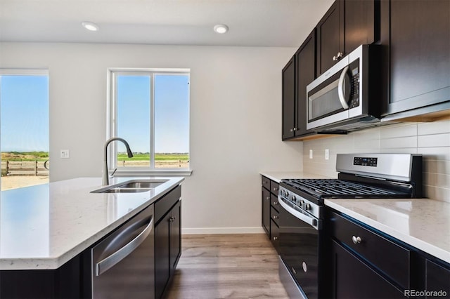 kitchen with light hardwood / wood-style flooring, appliances with stainless steel finishes, light stone countertops, sink, and decorative backsplash