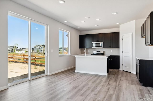 kitchen featuring a center island with sink, tasteful backsplash, appliances with stainless steel finishes, and light hardwood / wood-style floors